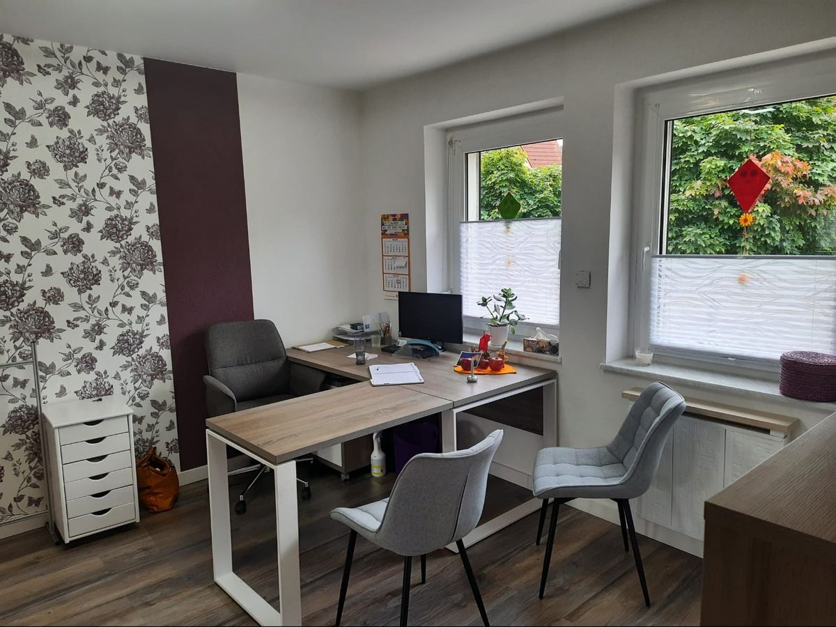 Behandlungszimmer mit Schreibtisch und Stühlen am Fenster