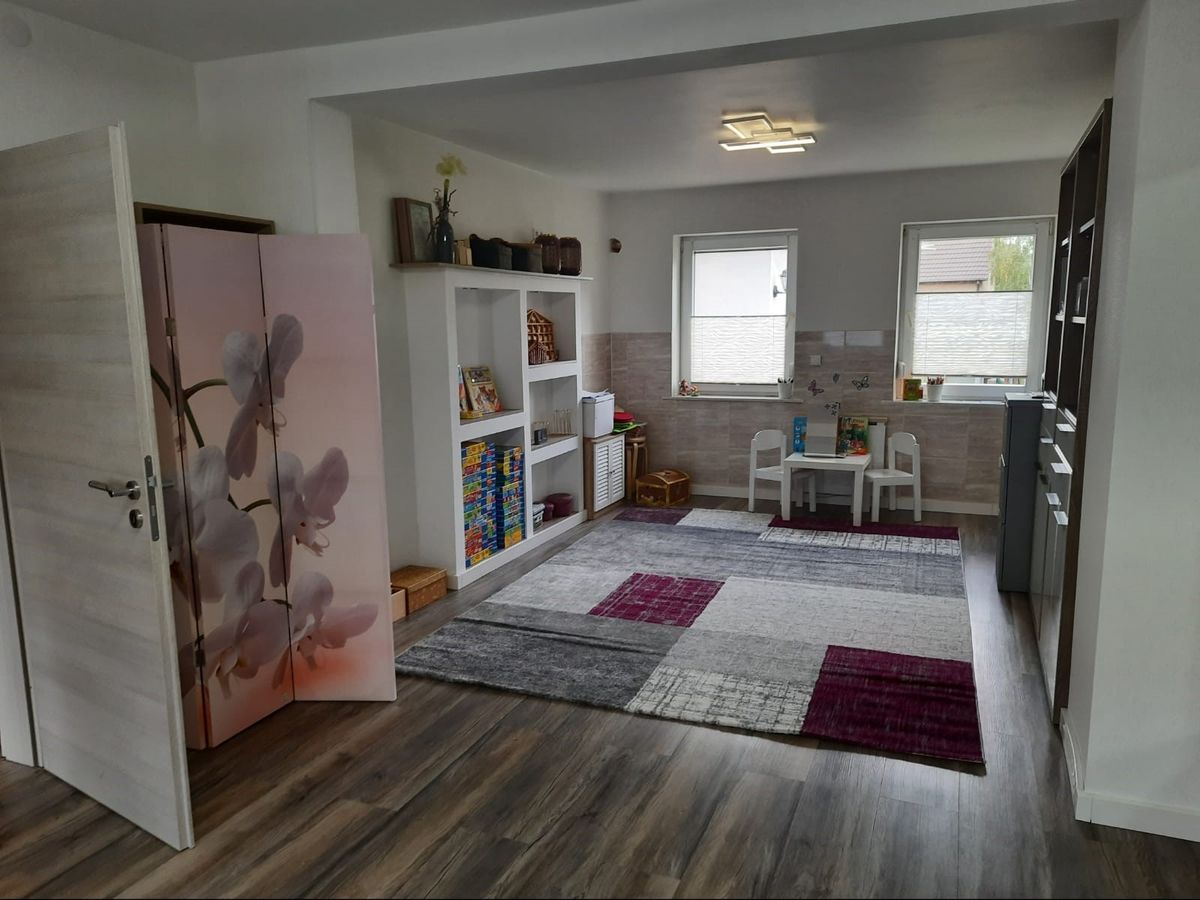 Therapieraum mit Spielteppich, Kindertisch und Regal mit Spielen